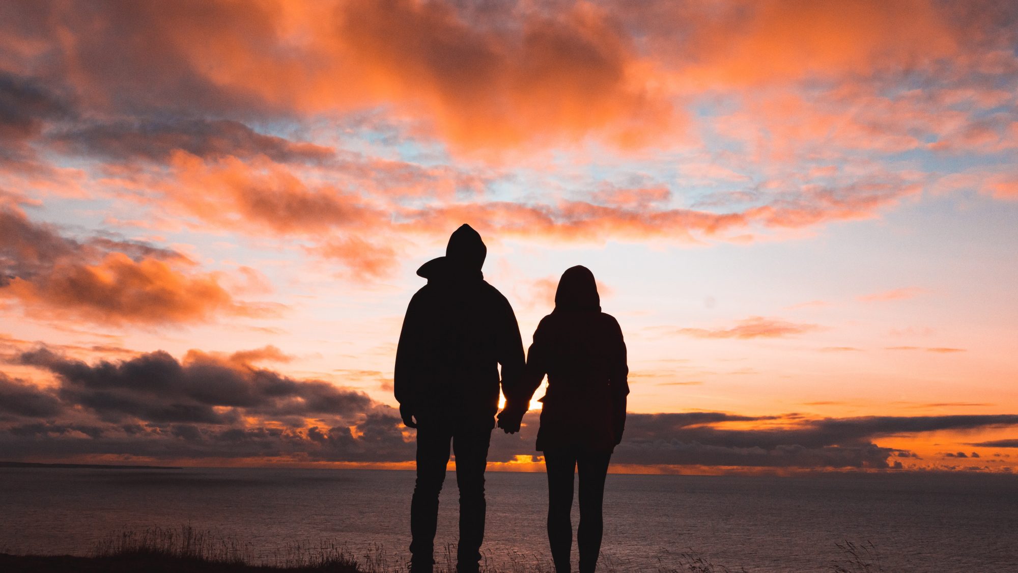silhouette photo of man and woman on cliff